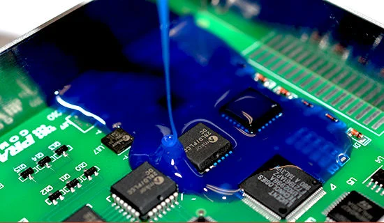 Blue epoxy compound being poured into electronic PCB assembly for complete component encapsulation and environmental protection